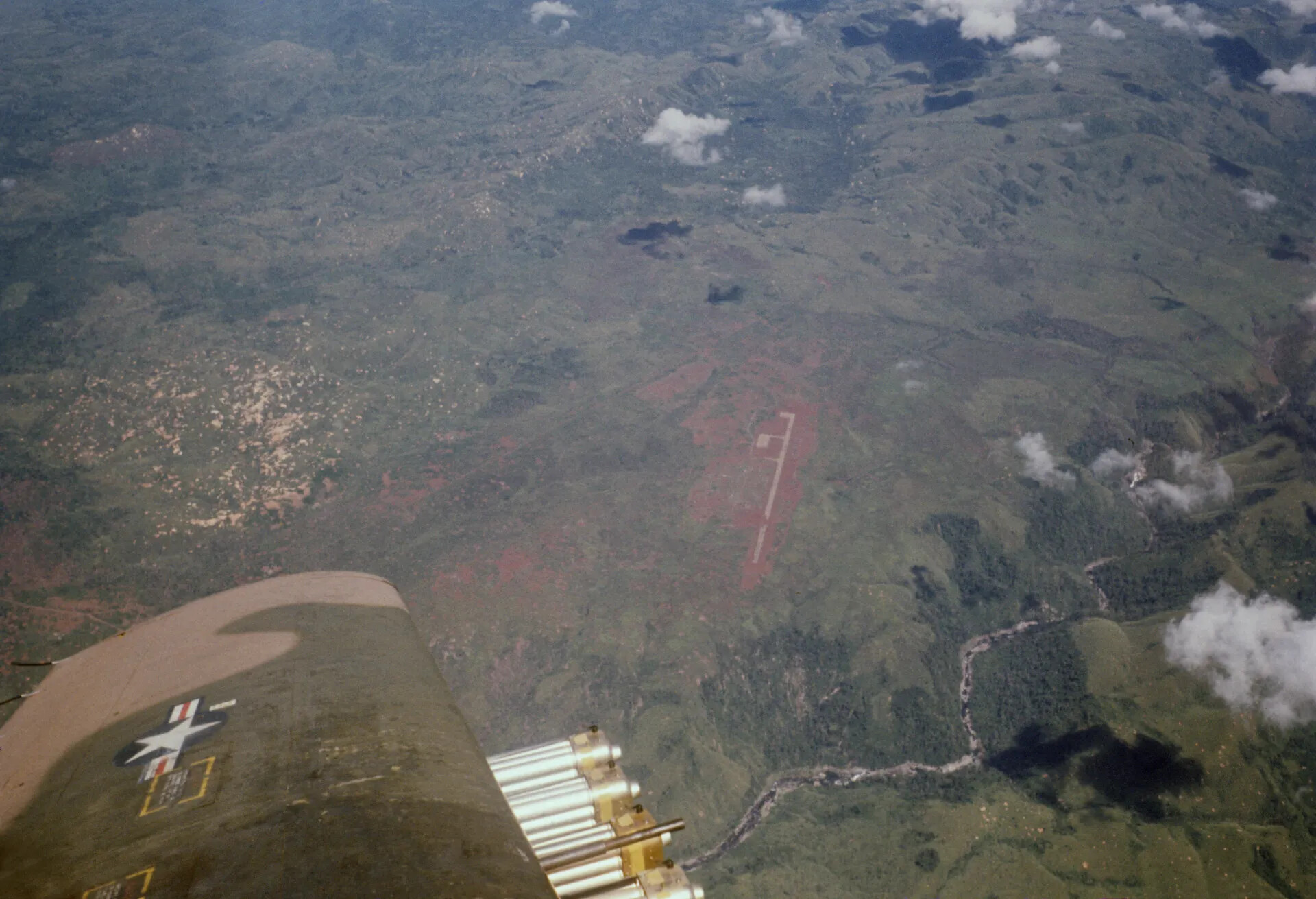 Cockpit View of Aircraft Wing with Rocket Pod Over Jungle Airstrip, Southeast Asia, circa 1970