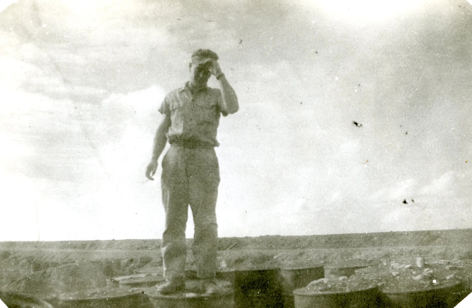 Serviceman Standing on Barrels, Shielding Eyes, Iwo Jima, WWII