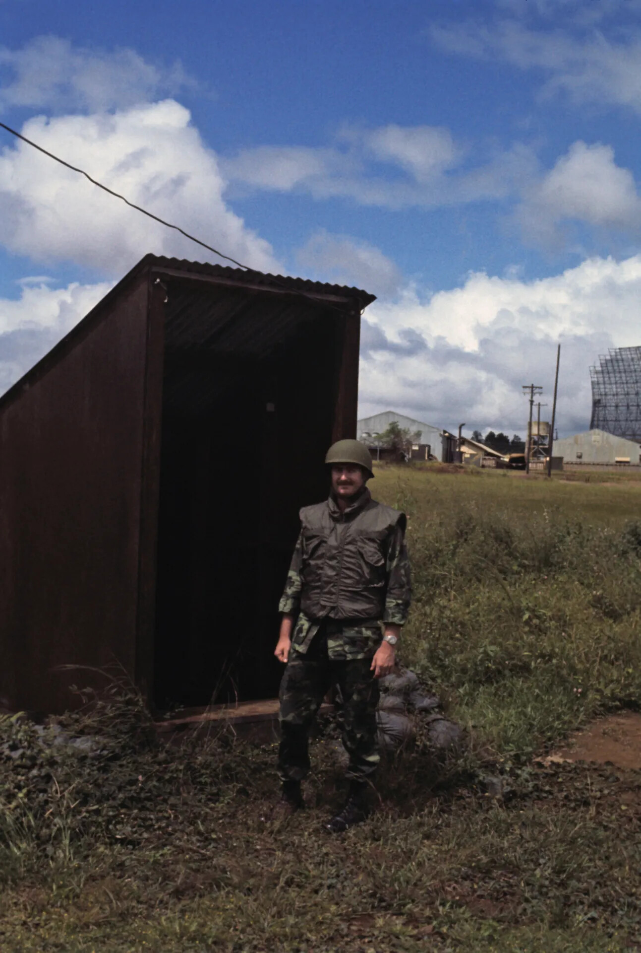 Airman in Helmet and Flak Vest Near Storage Bunker, Radar Site in Background