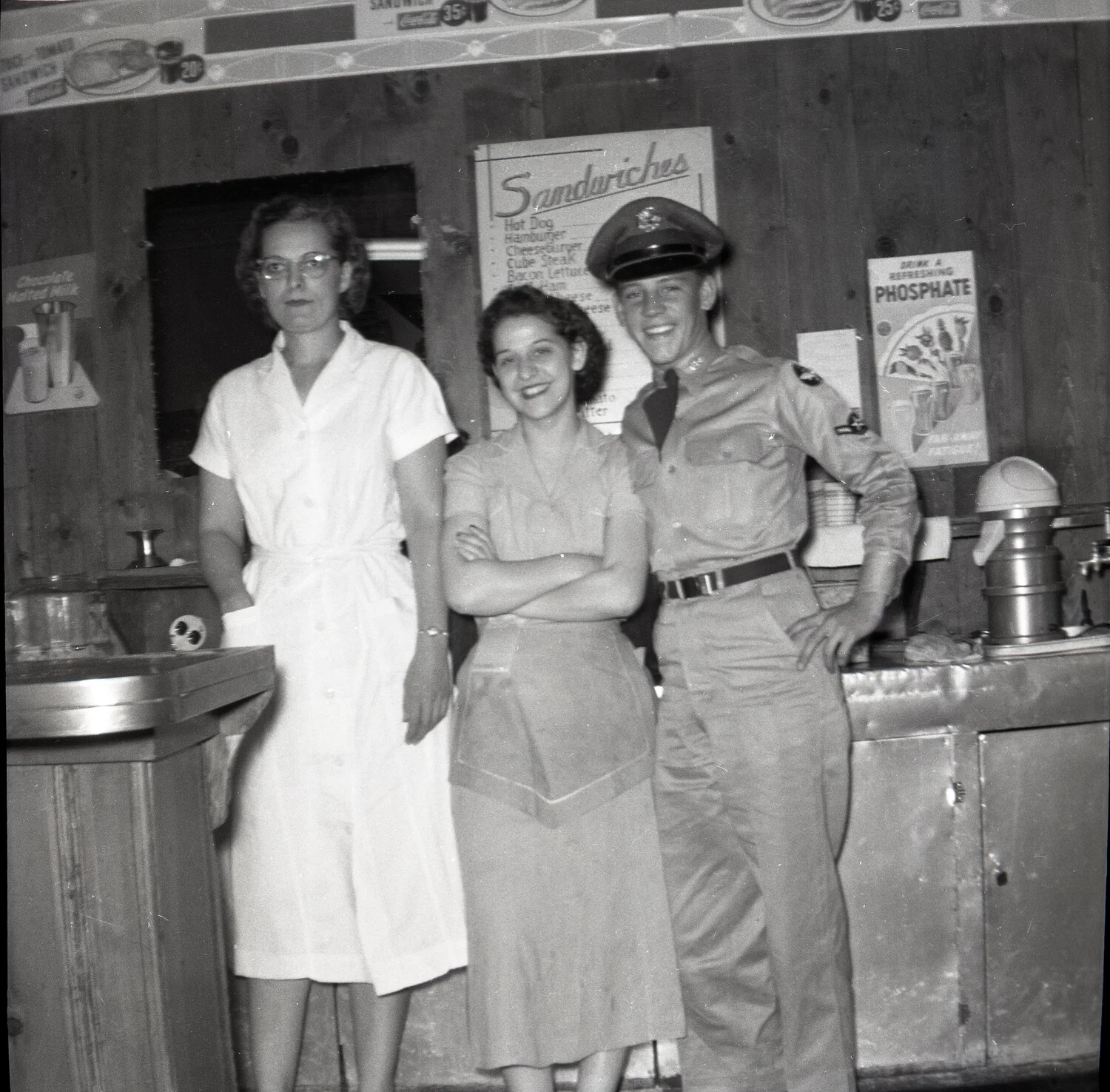 Airman Posing with Snack Bar Staff Beneath Menu Board, USAF Base, 1950s