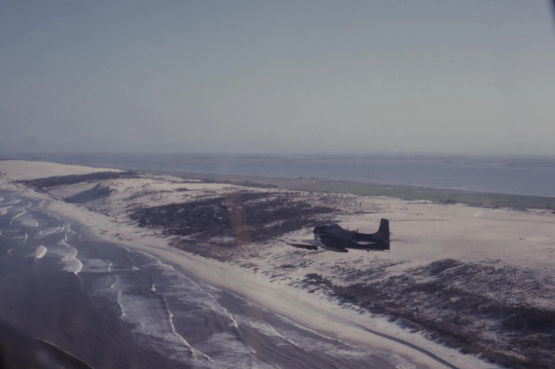 Air-to-Air View of a Douglas A-1 Skyraider Flying Low Over a Coastal Barrier Beach and Lagoon — Vietnam-Era Colour Slide