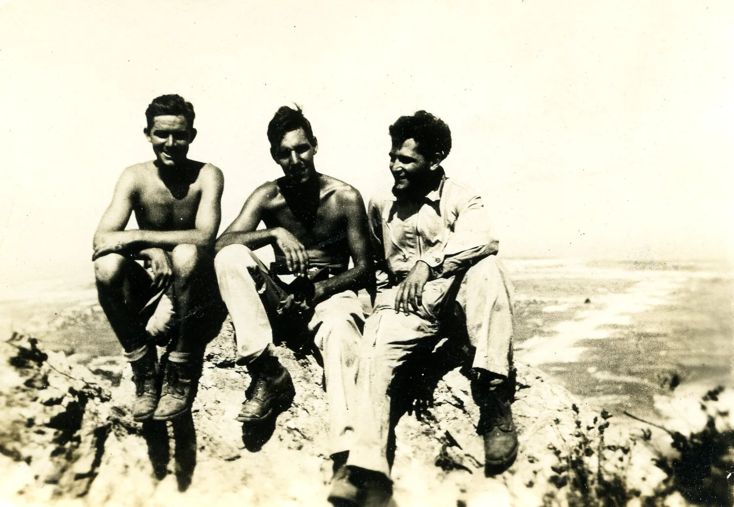 Three Servicemen Seated on a Coastal Cliff Overlooking the Shoreline