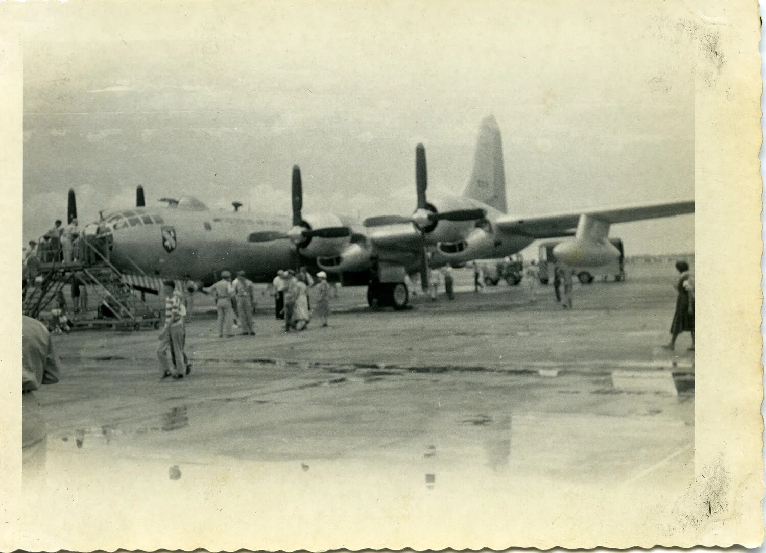 Ground Crew and Visitors Gathered Around B-29/B-50 Superfortress-Type Bomber on Wet Airfield Ramp