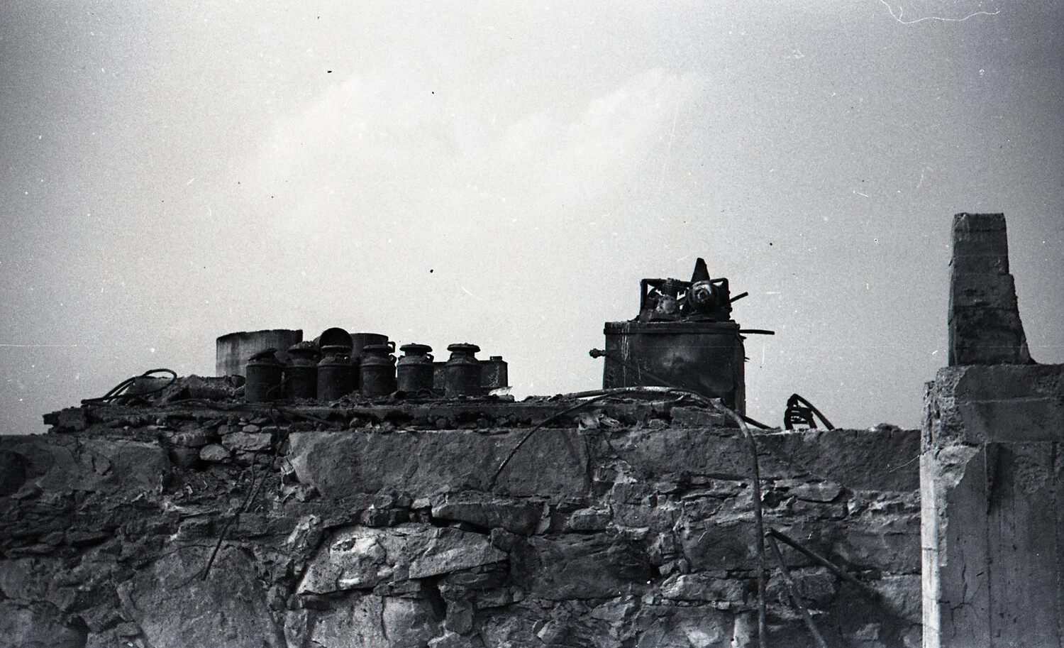 Surviving Milk Cans and Burned Dairy Equipment Atop Stone Wall
