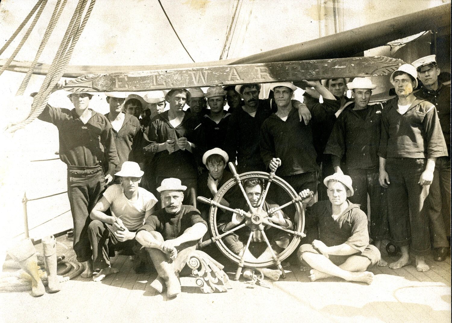 "The Heroes of the Wreck" -- Detail View of Crew Portrait with Salvaged Ship's Wheel and Nameboard, USS Columbia Album, c. 1900-1910
