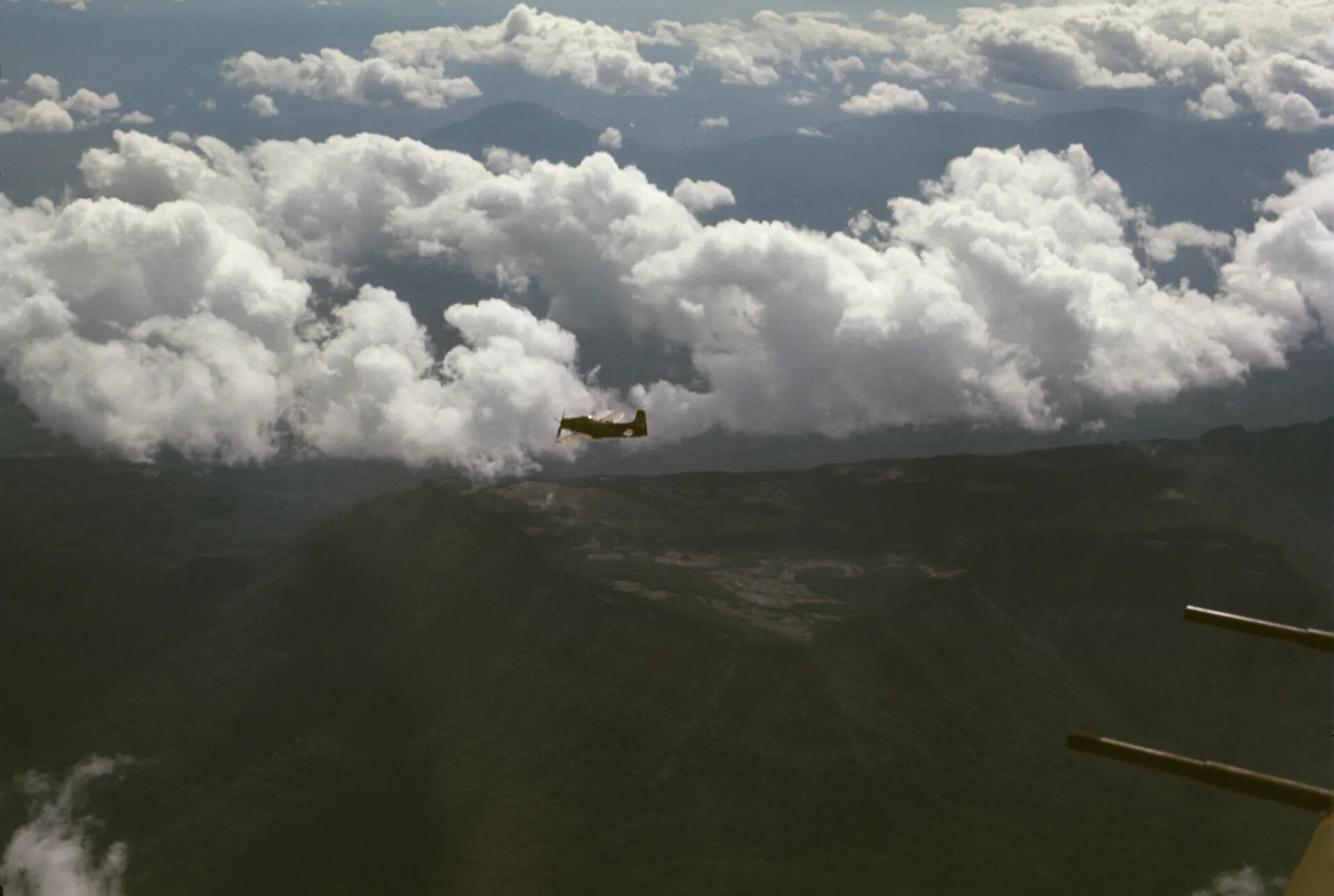 A-1 Skyraider in Flight Over Mountainous Terrain Beneath Towering Cumulus Clouds