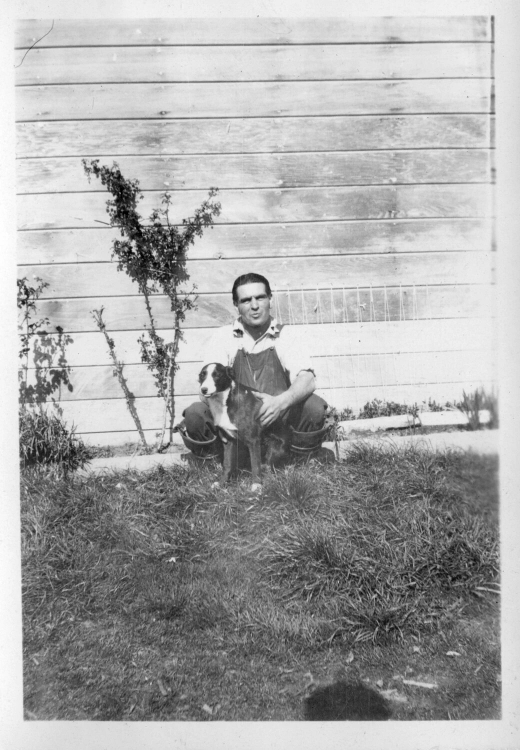 Man Holding a Puppy Beside a Farmhouse Wall, circa 1920-1928