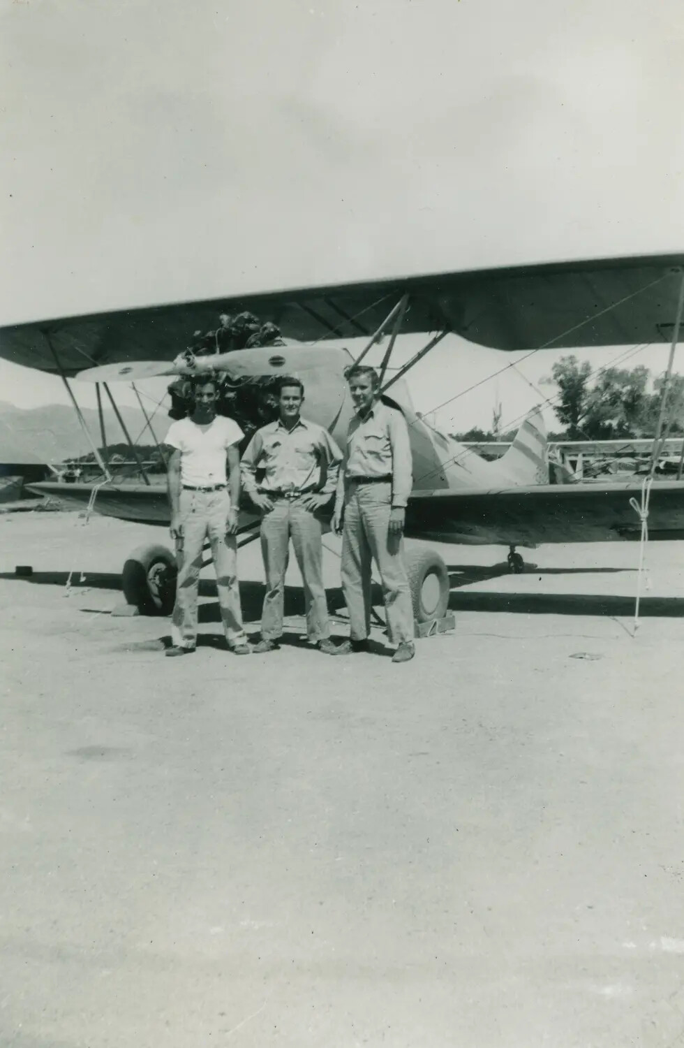 Three Men Posing with Biplane Trainer Aircraft at Airfield, WWII-Era Flight Training Facility