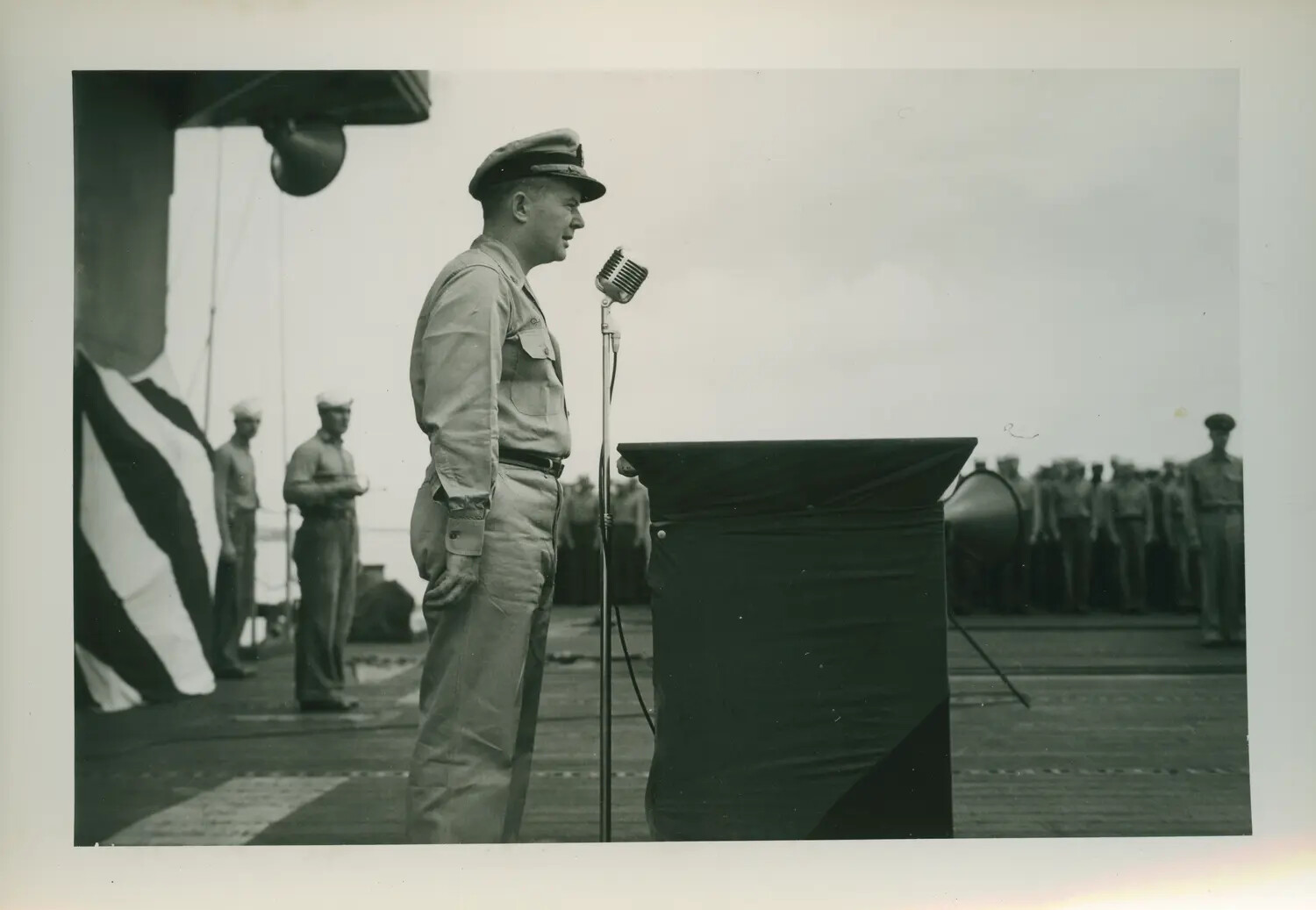 Officer Addressing Assembled Crew from Podium Aboard USS Petrof Bay (CVE-80)
