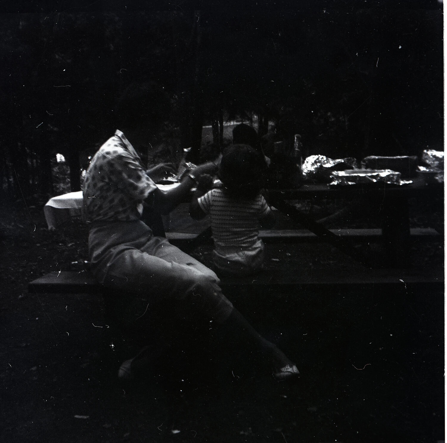 Man and Child Seated at Picnic Table with Foil-Wrapped Food, Mid-20th Century