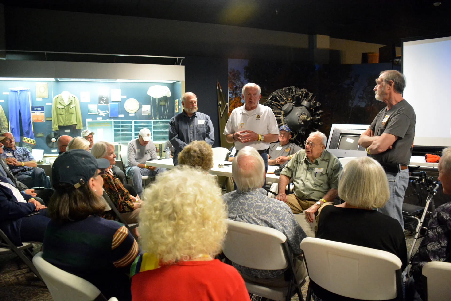 Veterans' Reunion Meeting, Aviation Museum — Speaker with Standing Group Near Uniform Display