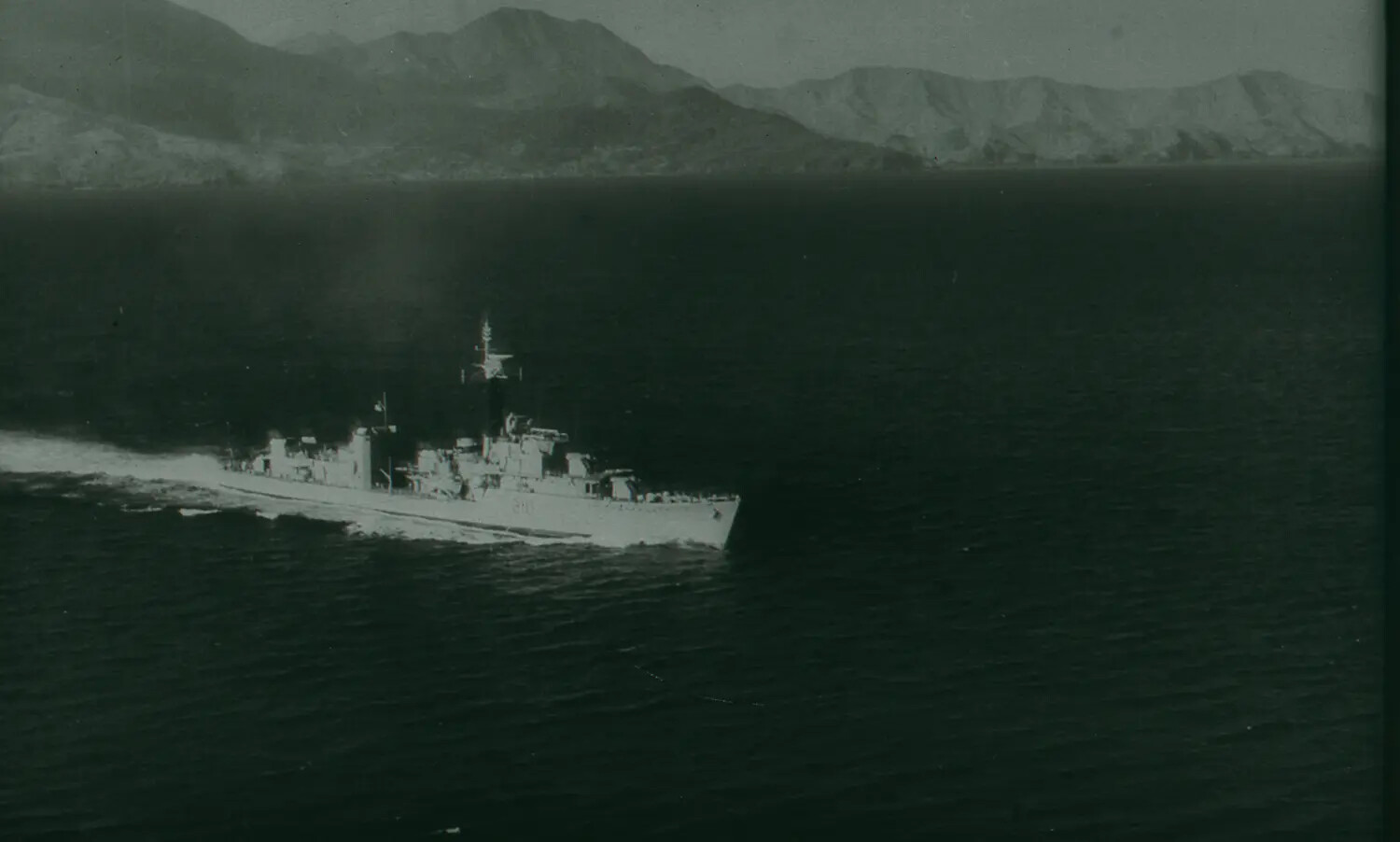 WWII-Era Warship Underway Off a Mountainous Coastline