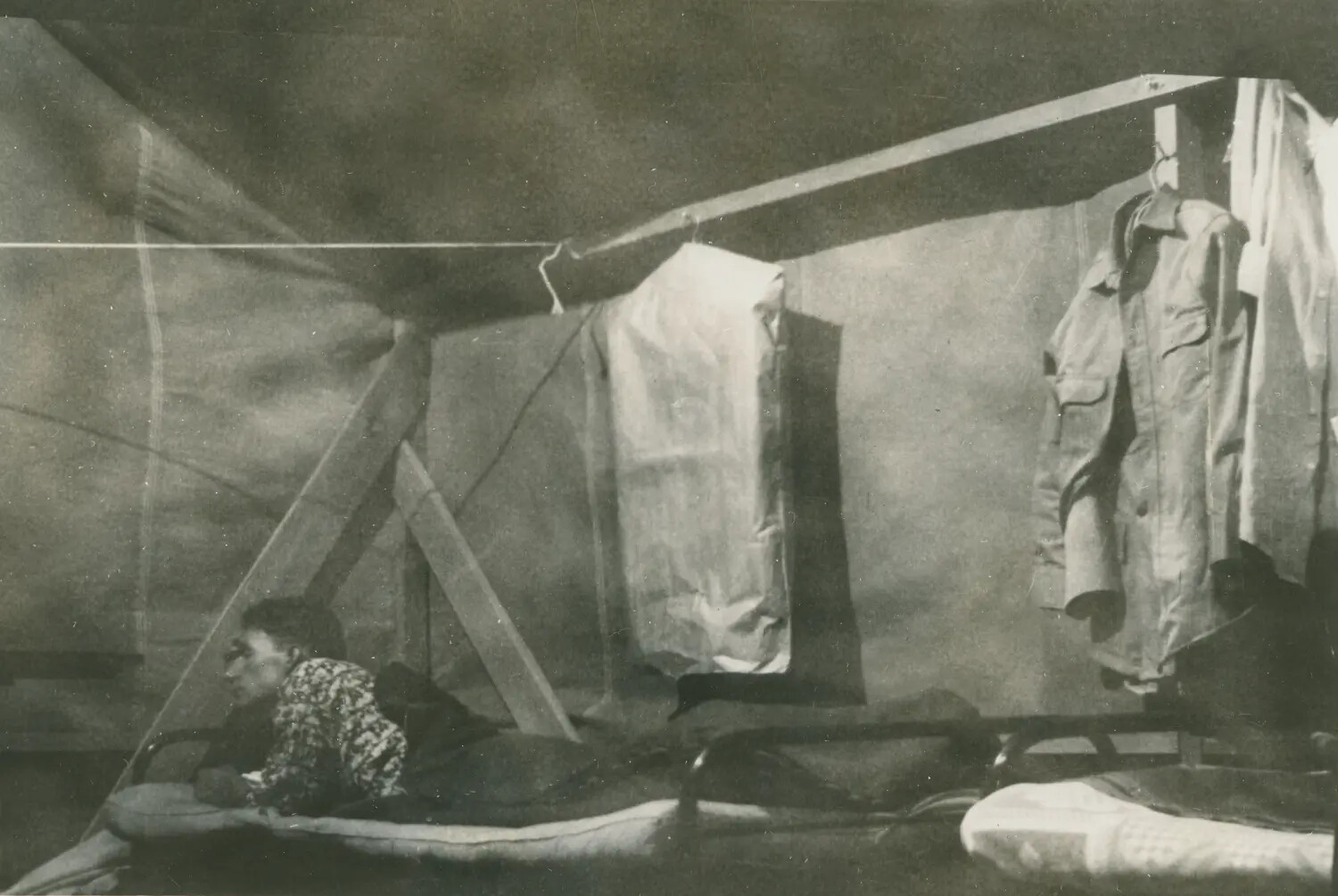 Serviceman in Tent Quarters with Hanging Uniforms and Folding Cots