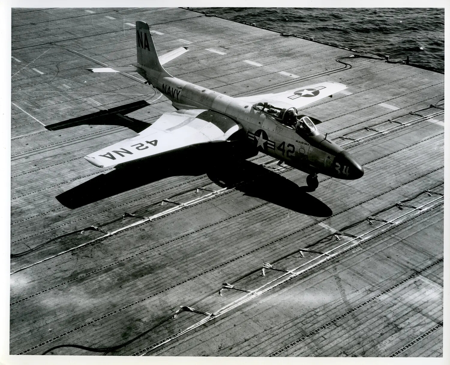 US Navy Swept-Wing Jet Fighter Banking Low Over an Aircraft Carrier Flight Deck