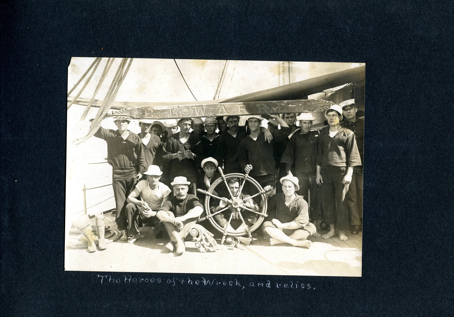 "The Heroes of the Wreck, and Relics" -- Crew Portrait with Salvaged Ship's Wheel and Nameboard, USS Columbia Album, c. 1900-1910
