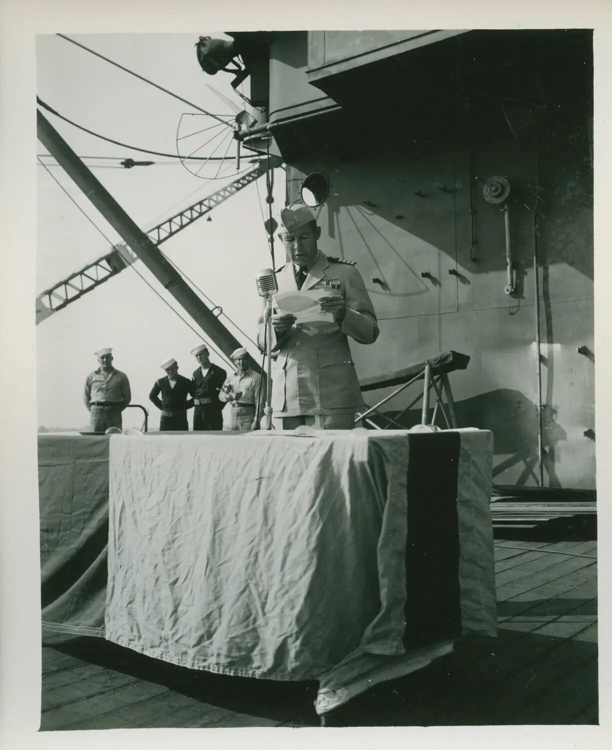 Shipboard Ceremony Aboard USS Petrof Bay (CVE-80) - Officer Addressing Crew at Podium