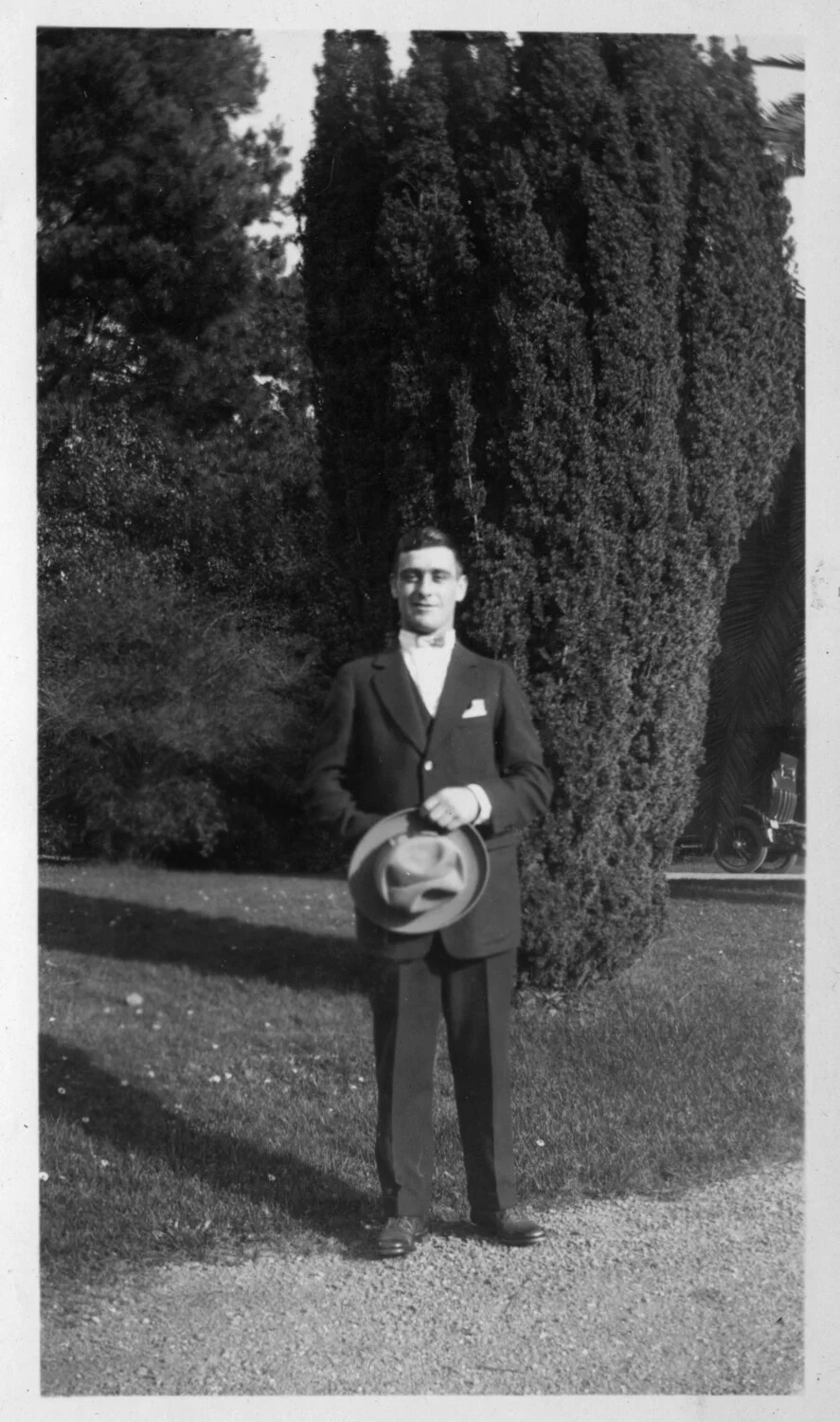 Young Man in Suit Holding Hat Beside Cypress Trees, c. 1920s