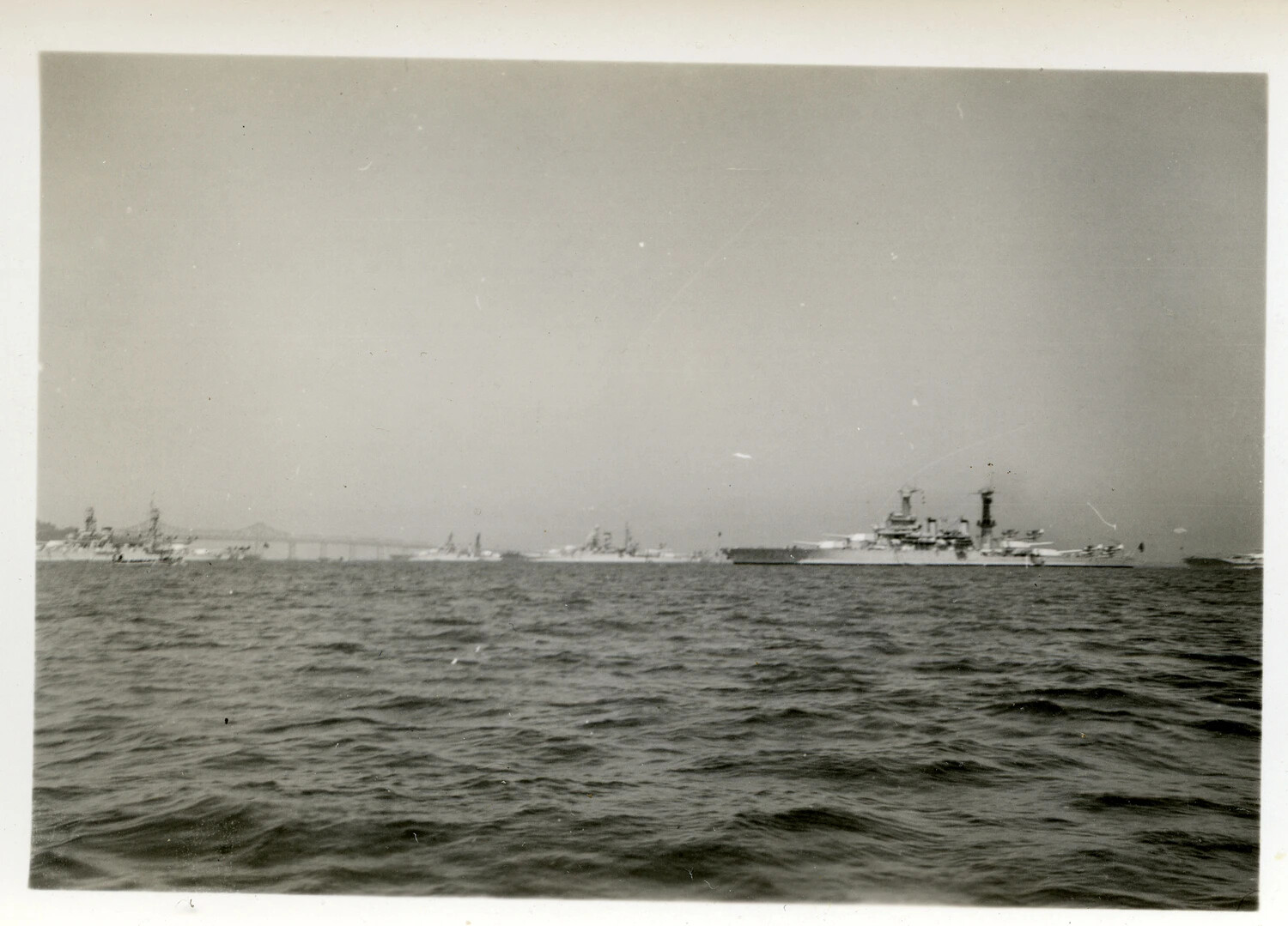 U.S. Navy Warships at Anchor Near a Truss Bridge, Pacific Coast Anchorage, World War II Era