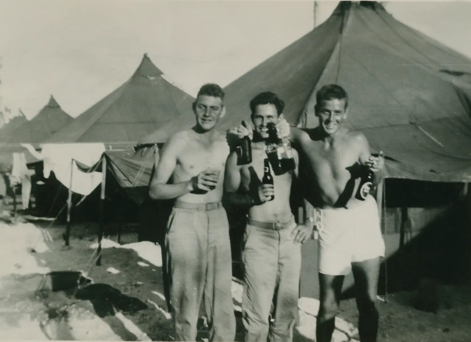 Three Servicemen Celebrating with Bottles at a Military Tent Encampment, Edward P. McAleer Collection, WWII Era
