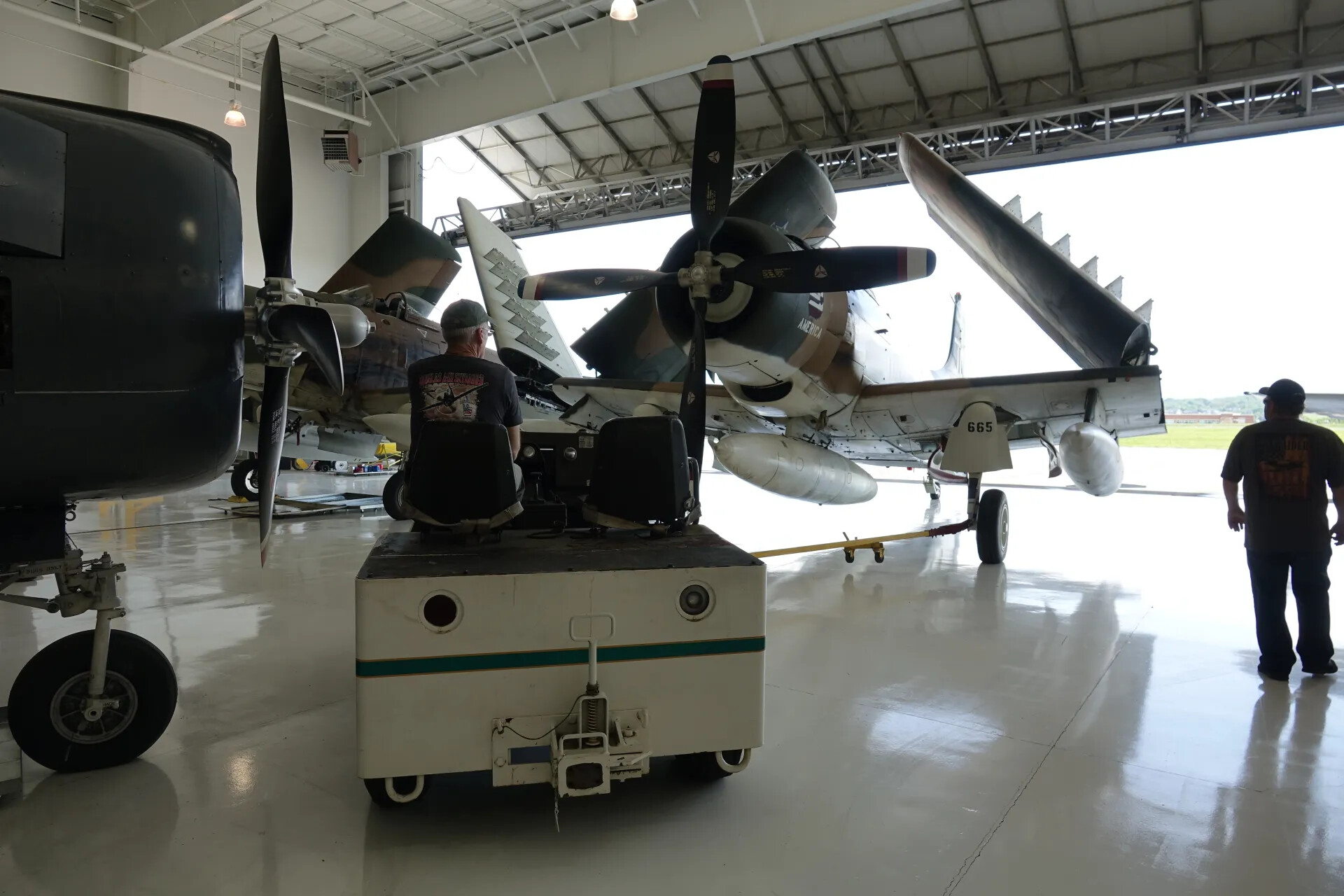 A-1 Skyraider 'America' (Tail 665) in Hangar with Ground Crew and Tow Tug