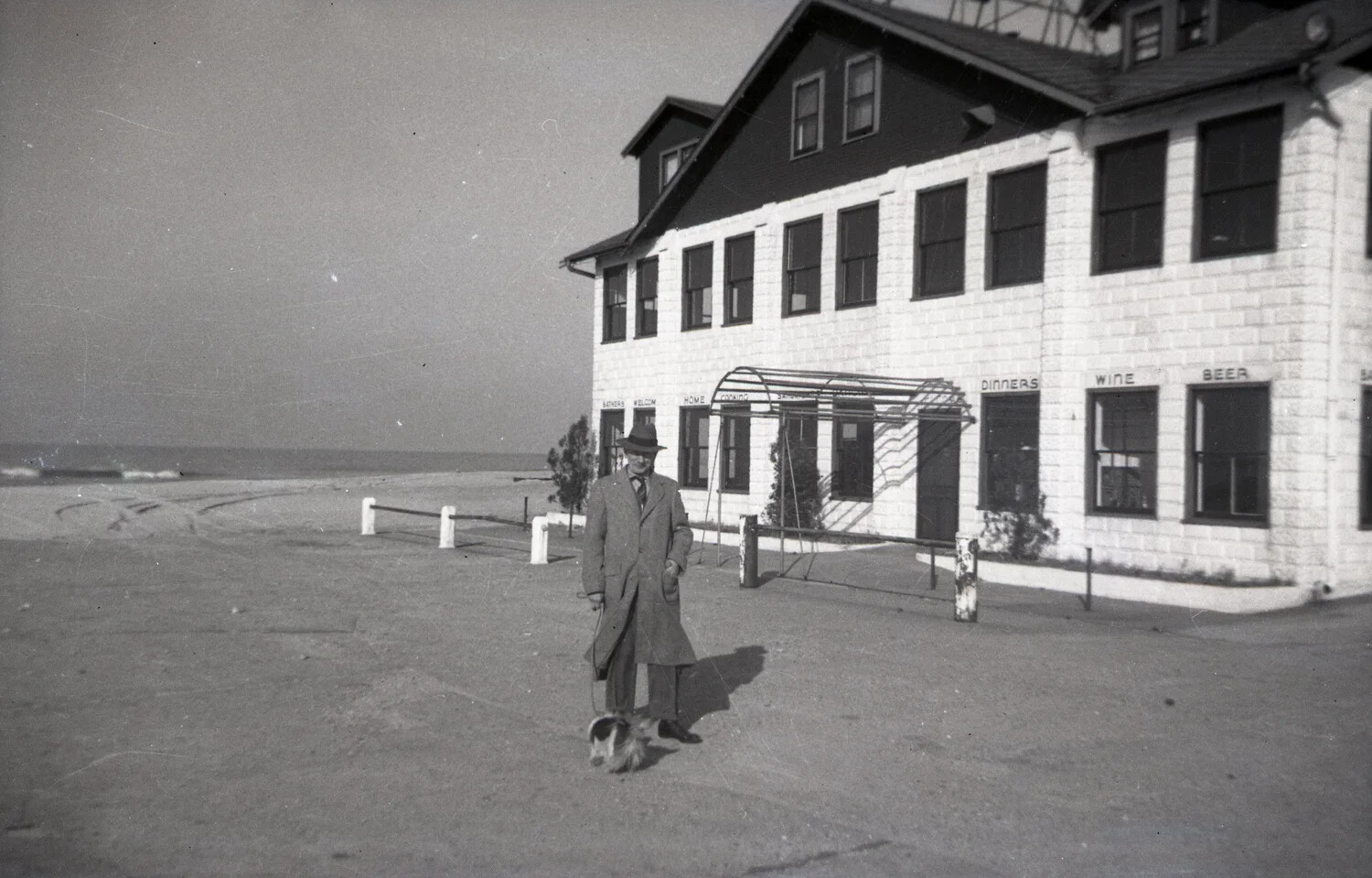 Man with Dog Outside Seaside Inn Advertising 'Bathers Welcome,' Coastal Resort Town