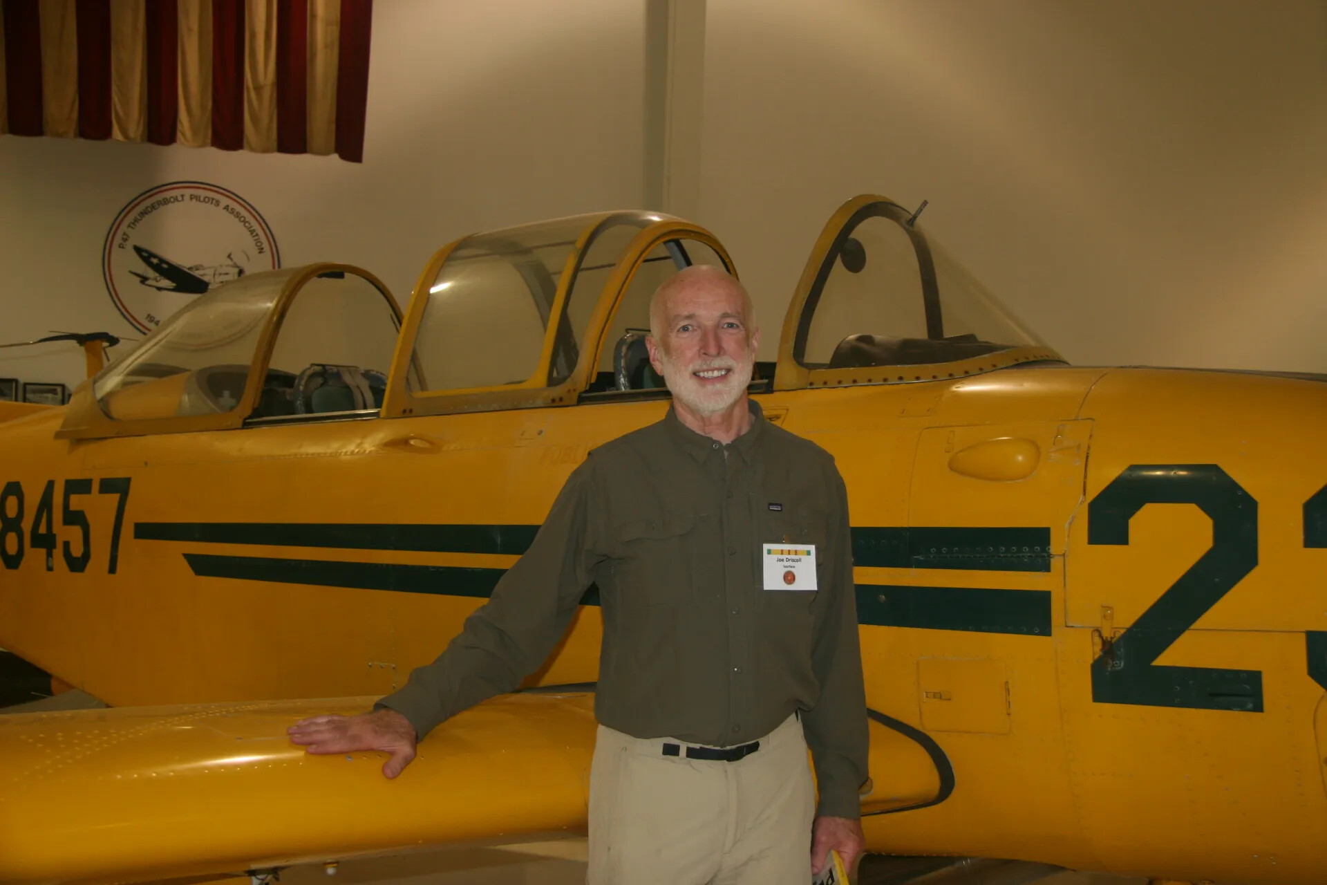 Veteran Joe Driscoll Beside Yellow Trainer Aircraft at Museum Event