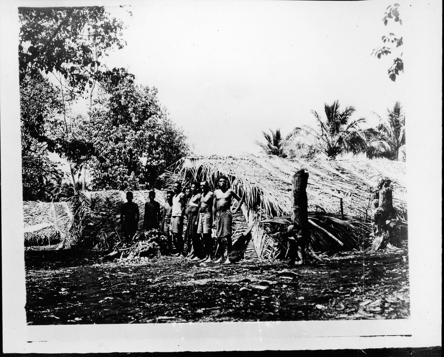 Group Portrait of Pacific Islander Men Before Thatched Dwelling