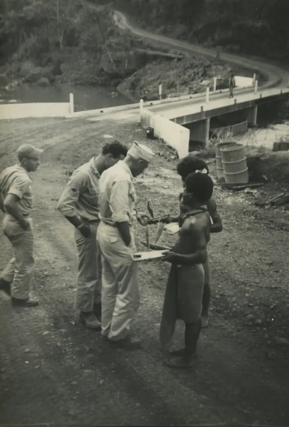 American Servicemen Trading with Local Villagers Near a Military Bridge