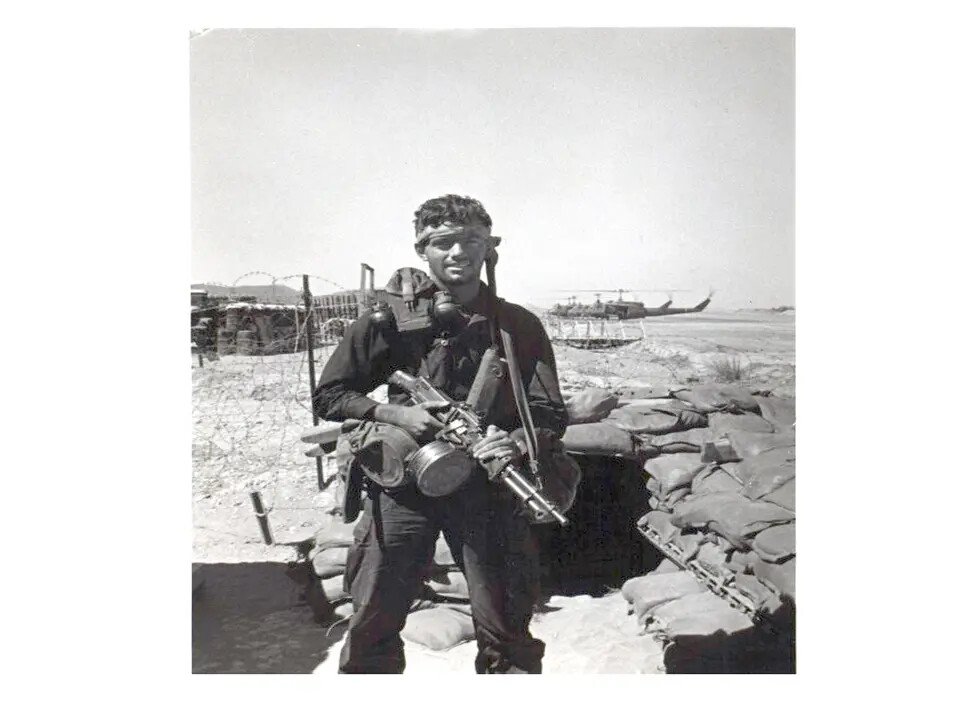 Serviceman with Captured Rifle at Sandbagged Bunker Position, Vietnam, with UH-1 Helicopters in Background
