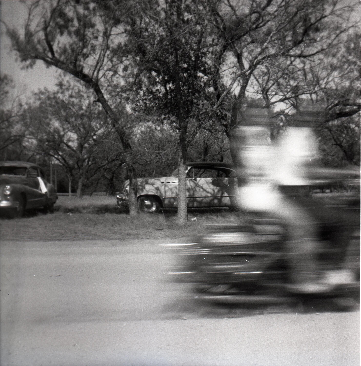 Motion-Blurred Snapshot of a Motorcyclist Passing Parked Automobiles on a Rural Roadside