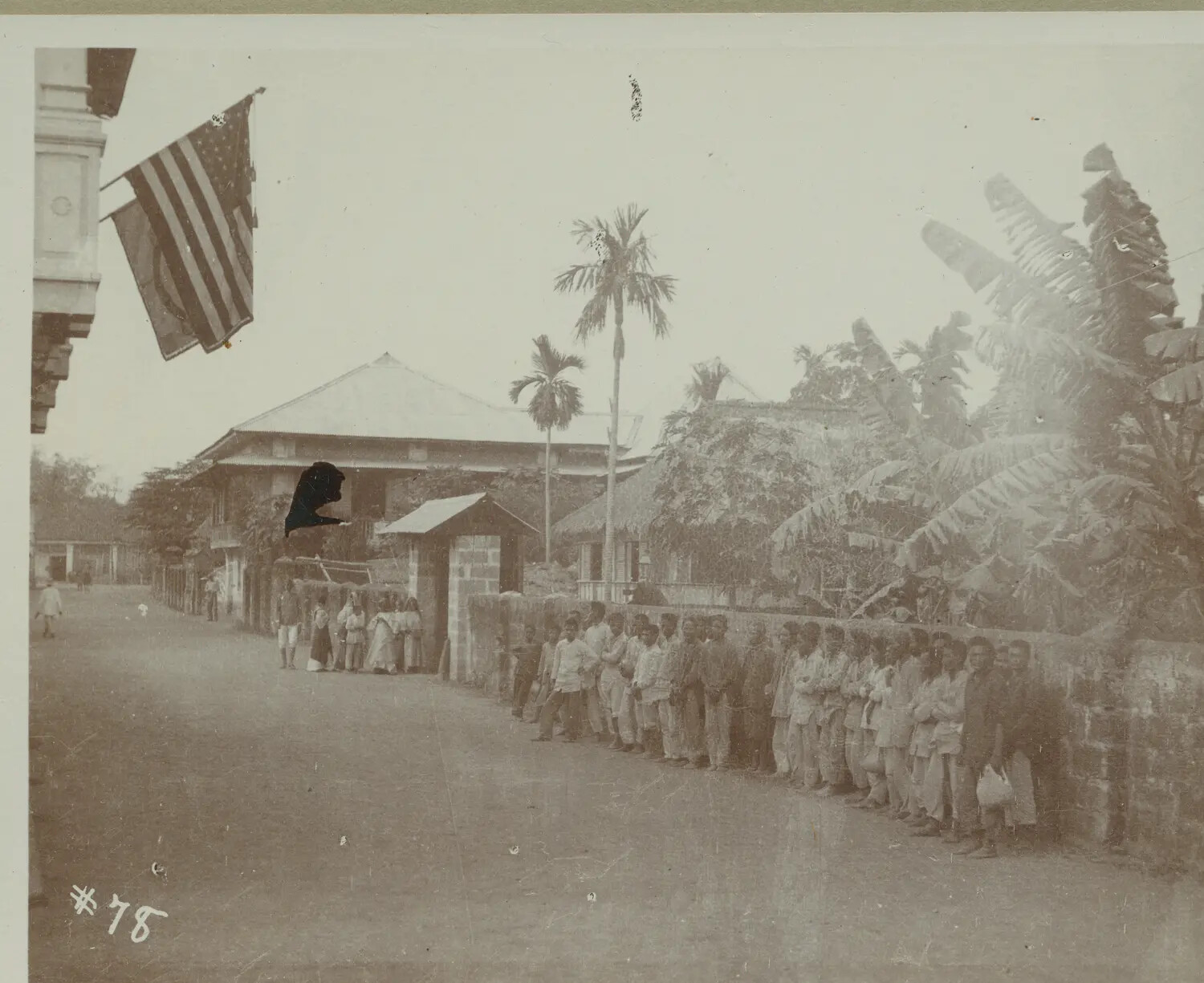 Street Scene with American Flag and Line of Filipino Men Along a Wall, Philippines, c. 1898-1900