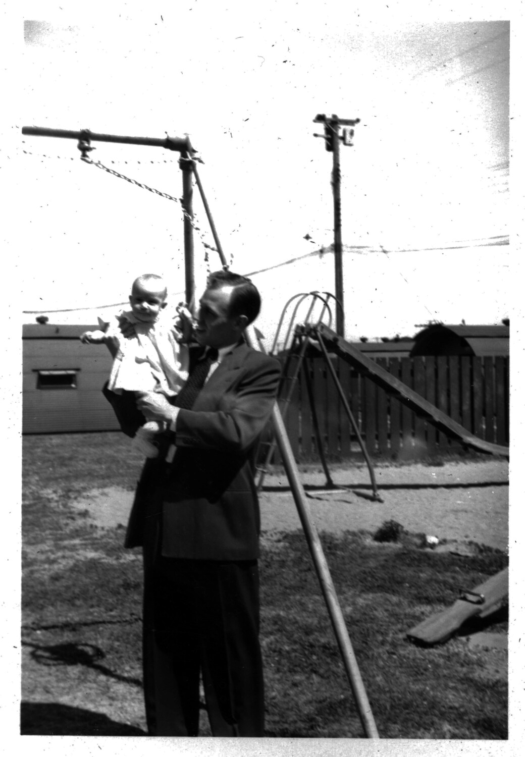 Man in Suit Holding Infant in Backyard, Home-Front Snapshot, c. 1950s