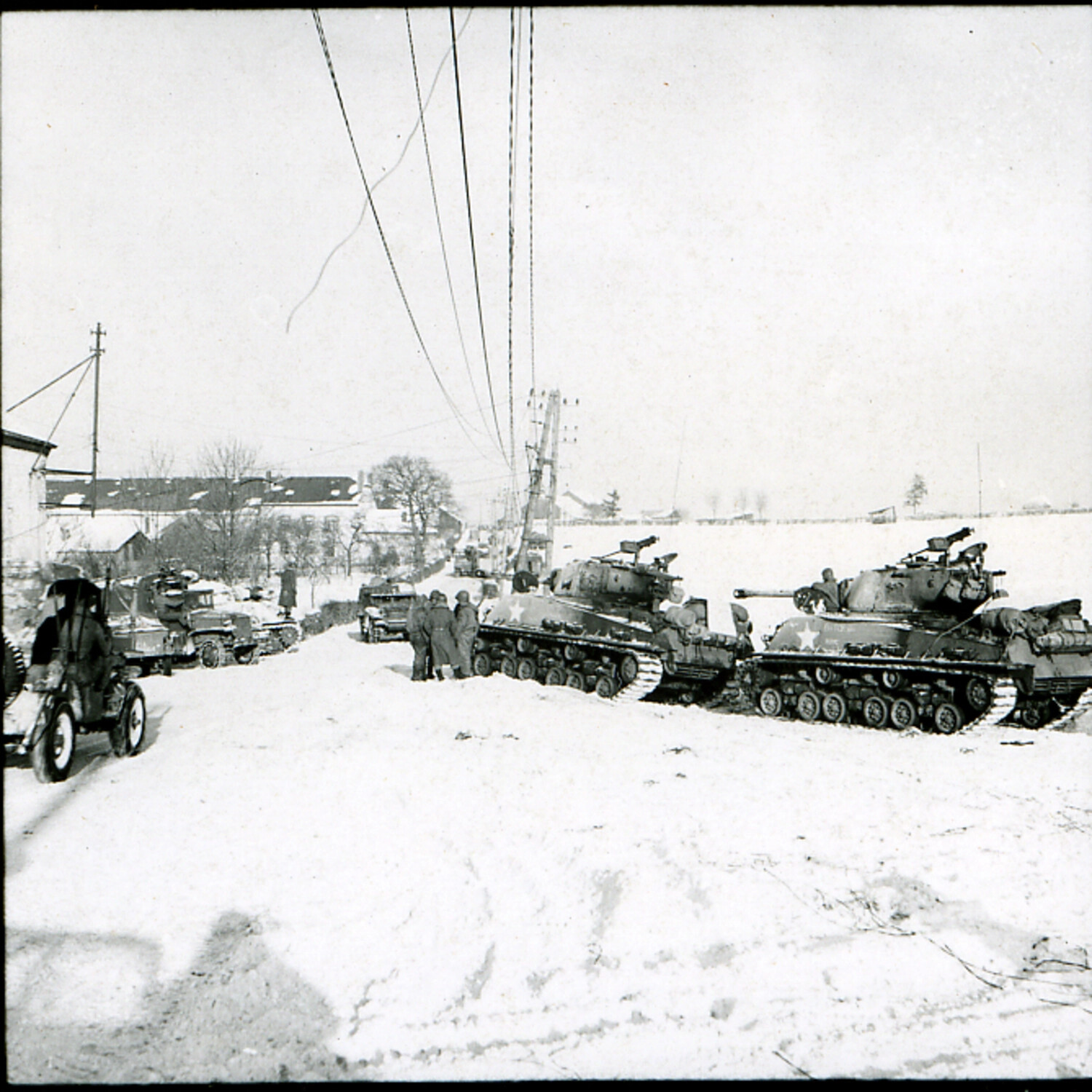 U.S. Army M4 Sherman Tank Column Halted in Snow-Covered European Village, Winter 1944-45 (Battle of the Bulge Era)