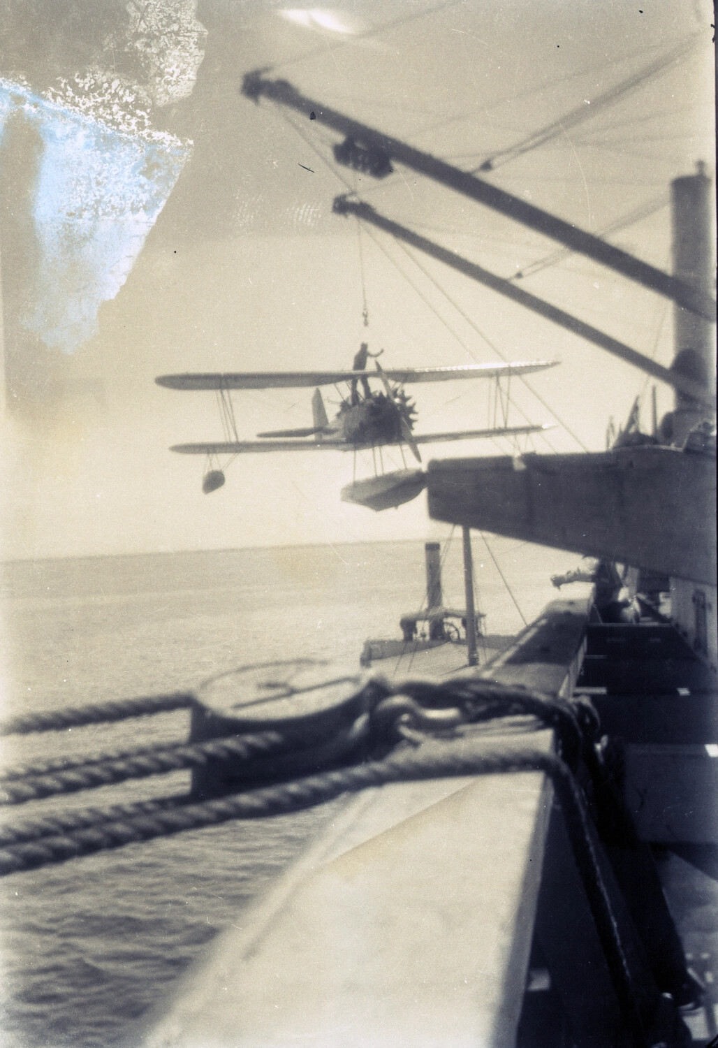 U.S. Navy Biplane Floatplane Being Hoisted by Shipboard Crane, China/Pacific Station, 1930s
