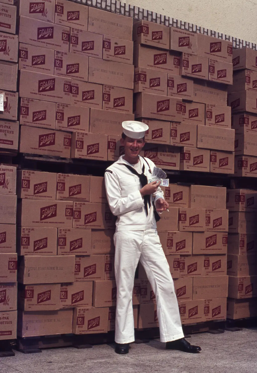 US Navy Sailor with Cash Winnings Amid Stacked Schlitz Beer Cases, Vietnam Era