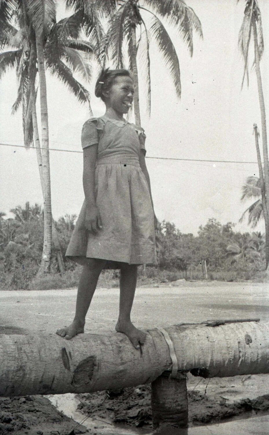 Filipina Girl Balancing on Coconut Log Footbridge, Luzon, Philippines, WWII Era