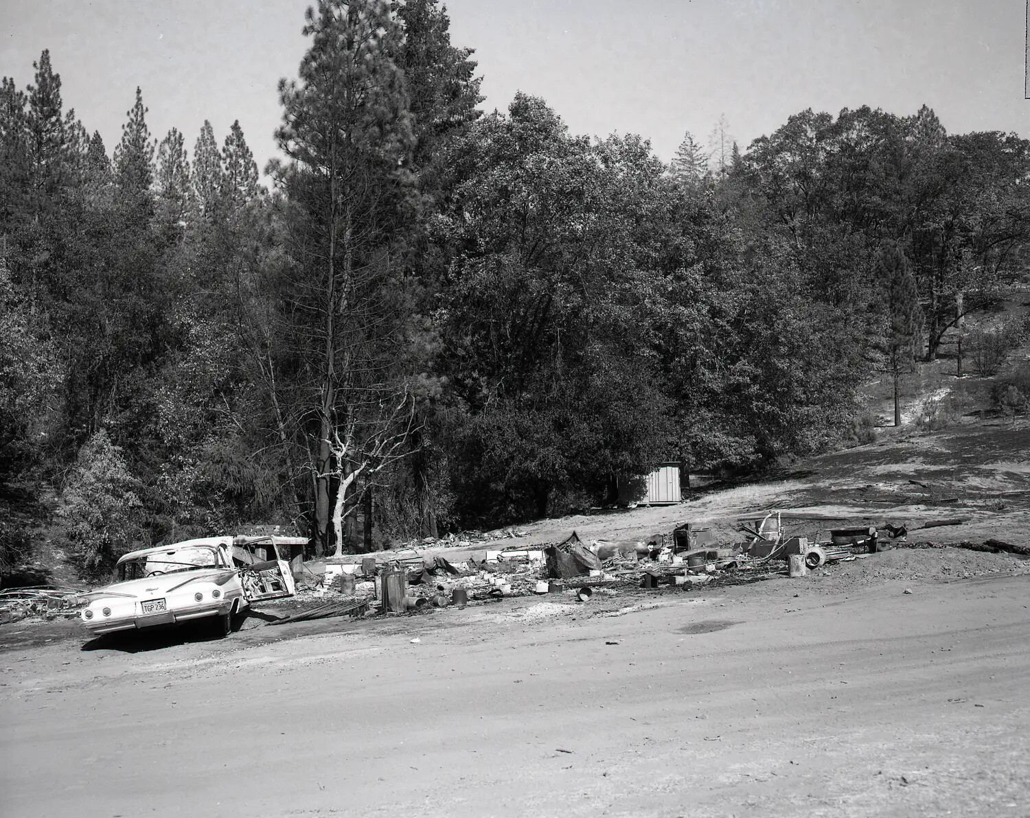Wide View of Fire-Damaged Property with Burned Vehicle and Debris Field