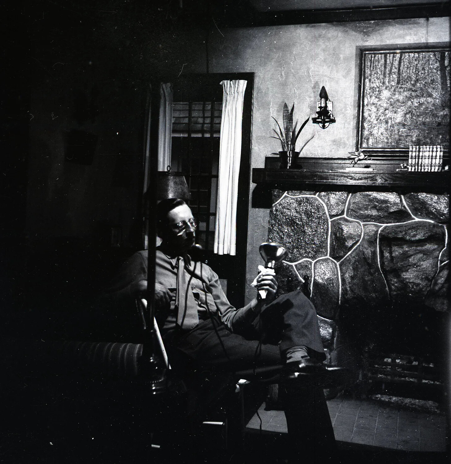 Man Seated by a Stone Fireplace Holding a Photoflood Reflector Lamp