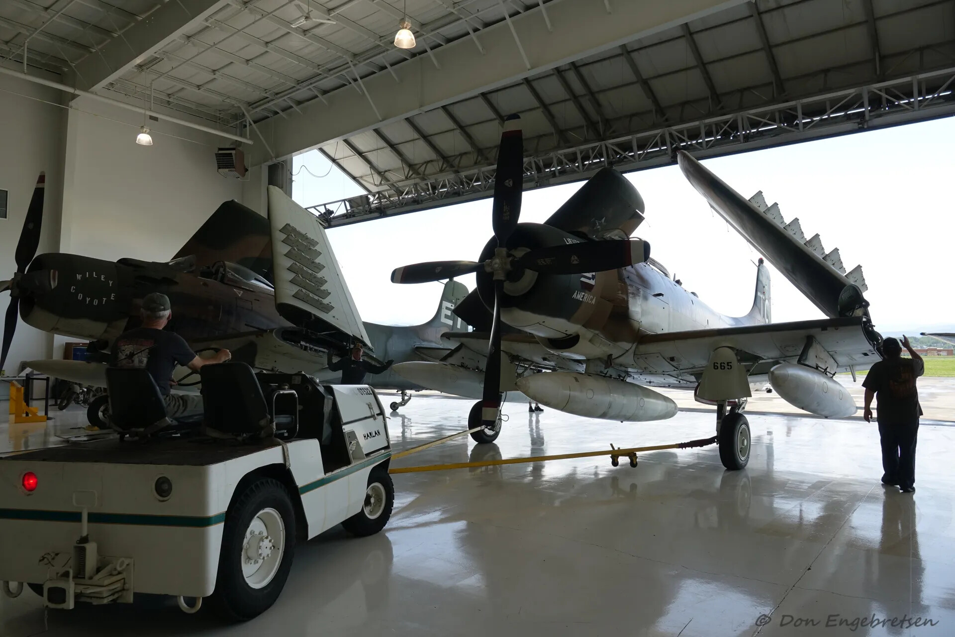 A-1 Skyraider 'Wiley Coyote' Towed Through Hangar Toward 'America 665' and 'ET' Skyraiders