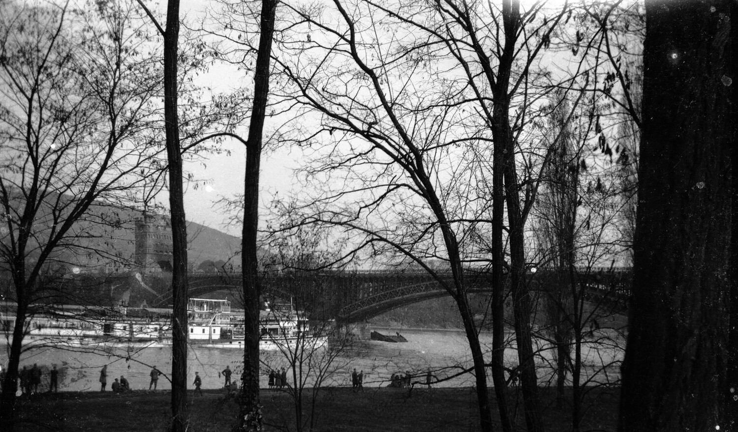 European River Scene with Arch Bridge, Stone Tower, and Riverboats, Viewed Through Bare Trees (WWI-Era Negative, Scott Field-England Collection)