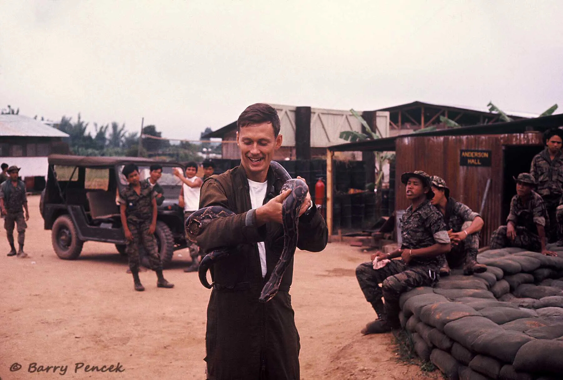 Serviceman Holding a Python at Base Camp, with Indigenous Troops and "Anderson Hall" Signage
