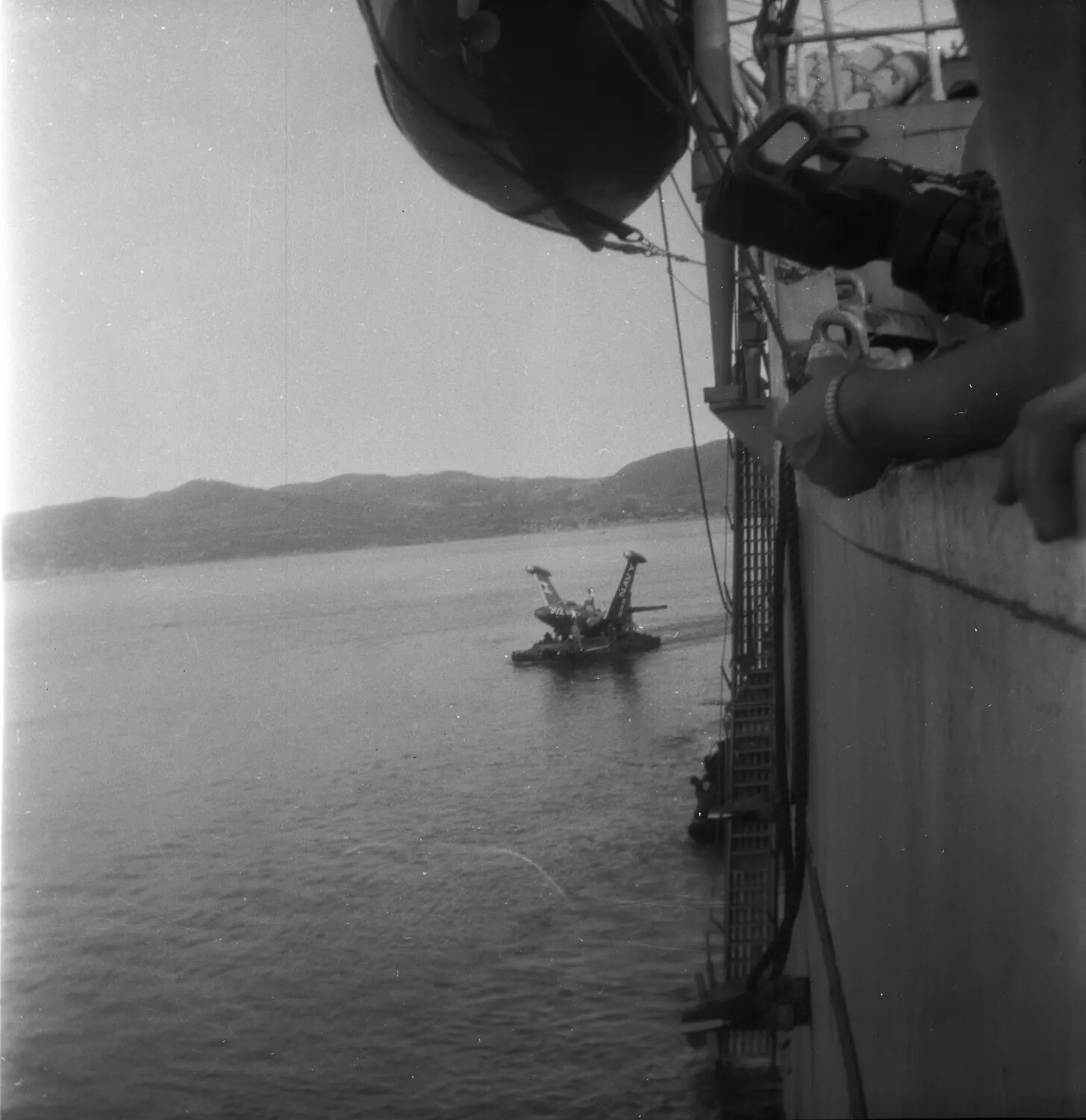 U.S. Navy Personnel Observing Twin-Finned Craft Marked 'NAVY' Alongside Ship, Sasebo Harbor, Japan