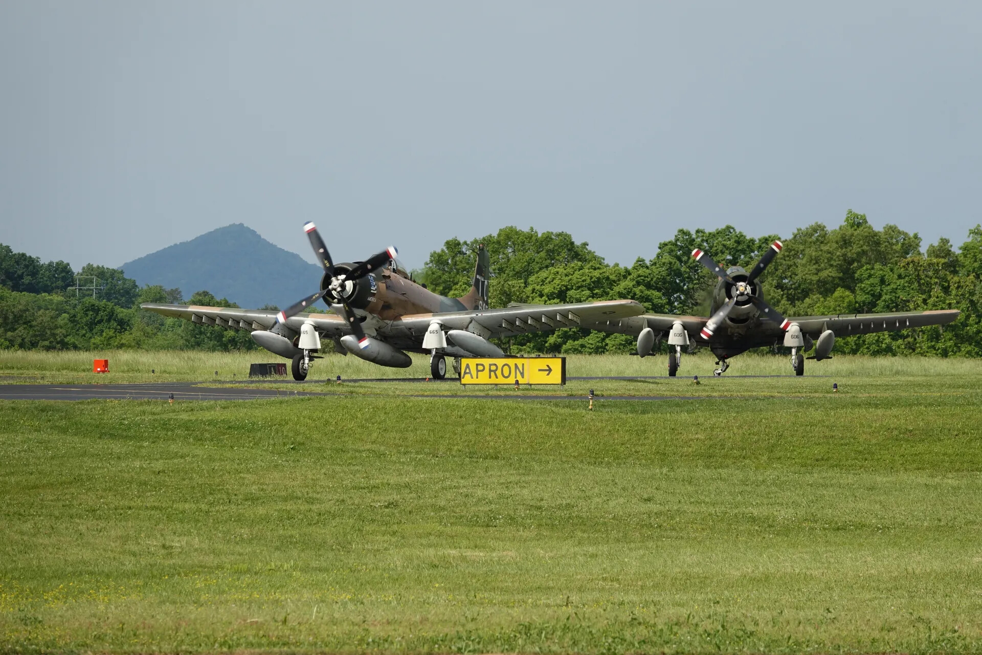 Two Douglas A-1 Skyraiders, Engines Running, Near Apron Taxiway Sign