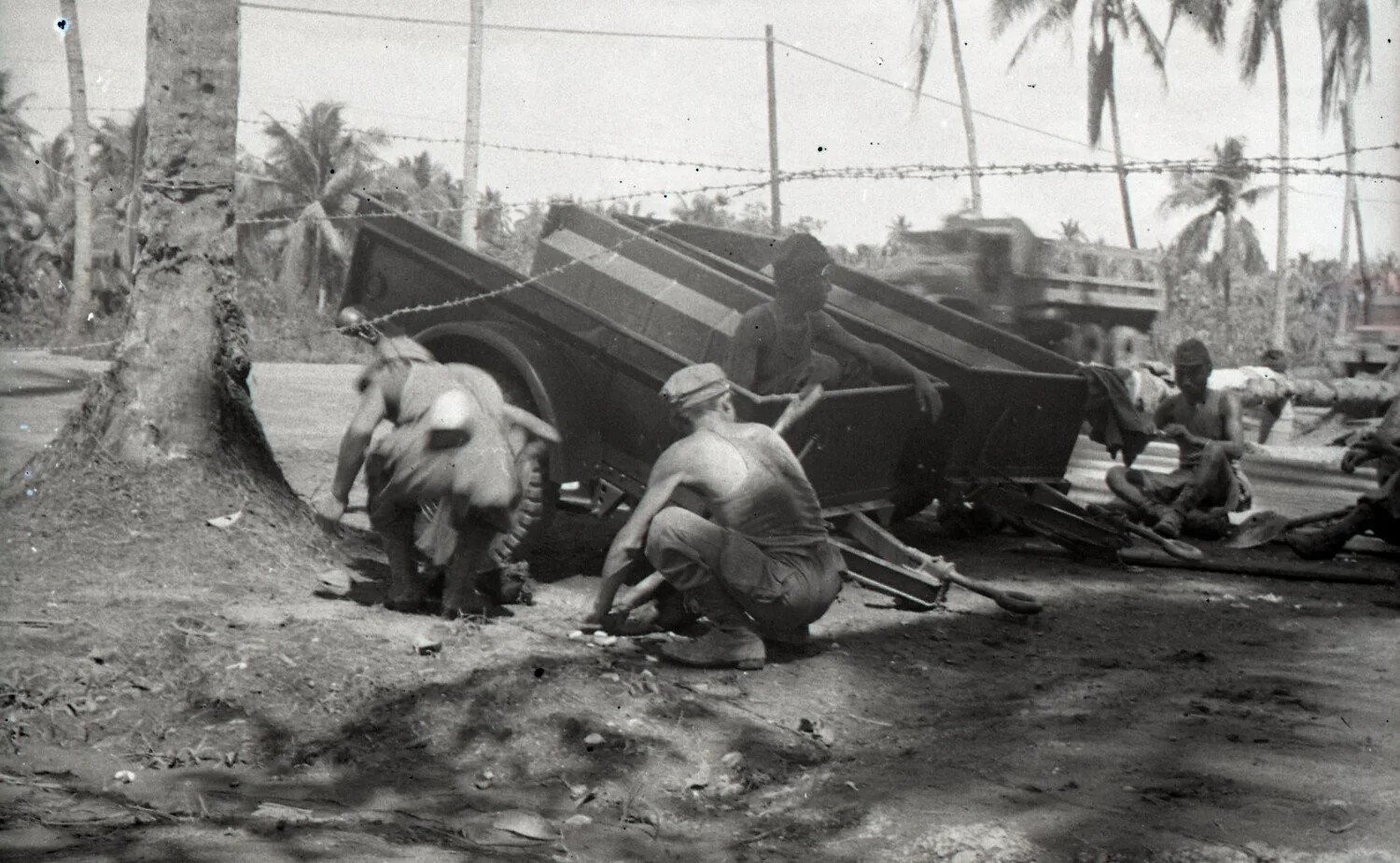 Servicemen Resting Beside Tilted Cargo Trailer Near Barbed Wire Fence, Luzon, Philippines, WWII