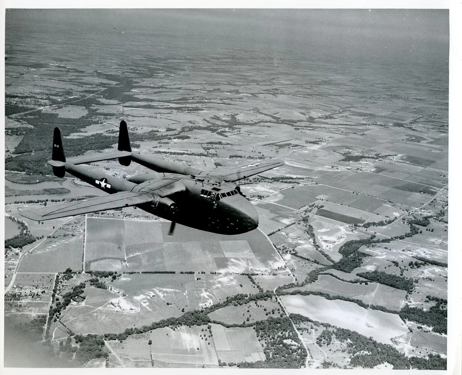 Twin-Boom Military Transport Aircraft in Flight Over Farmland
