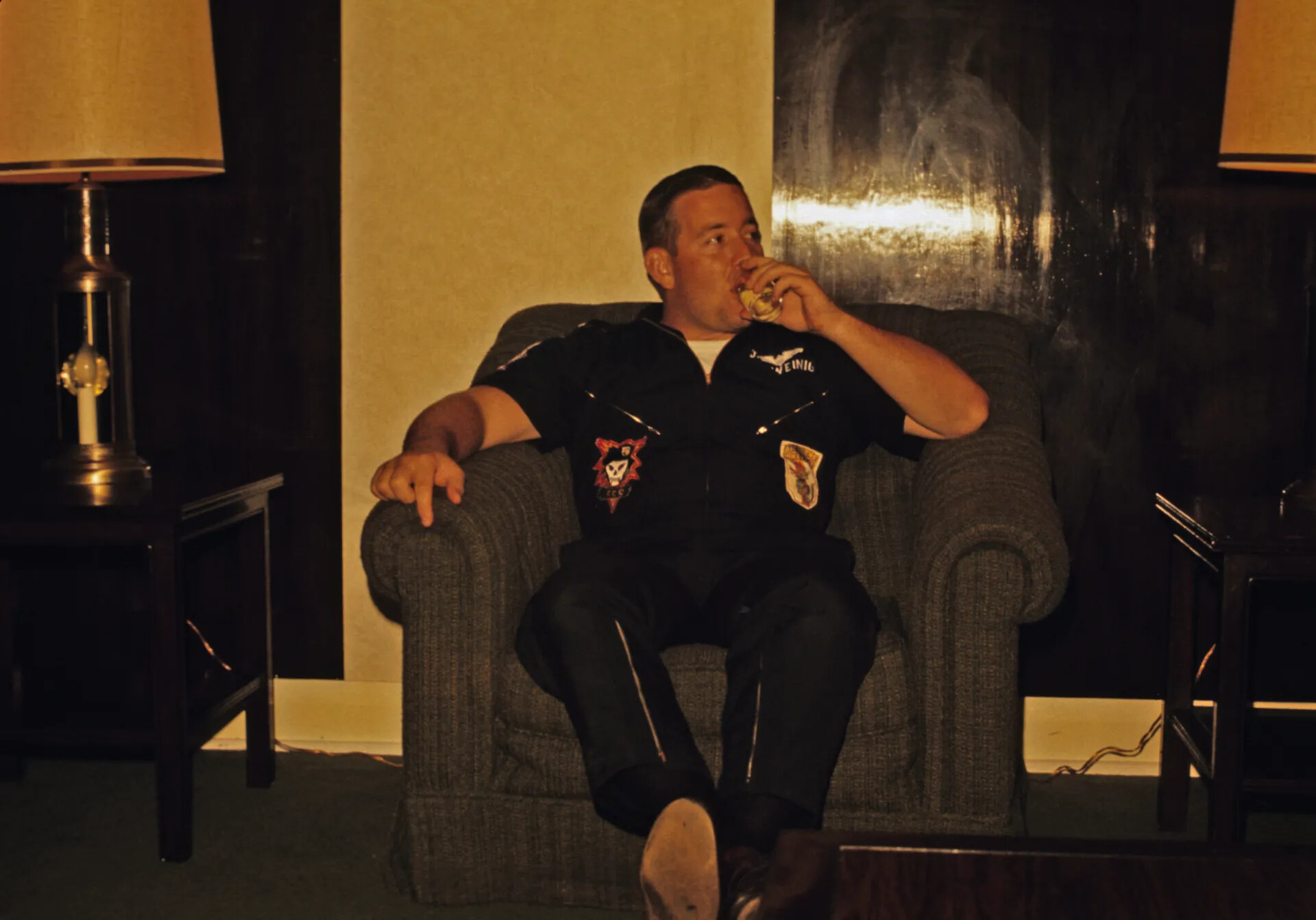 Man in Black Squadron Party Suit with SOG-Style Skull Patch, Seated at Home, circa 1970