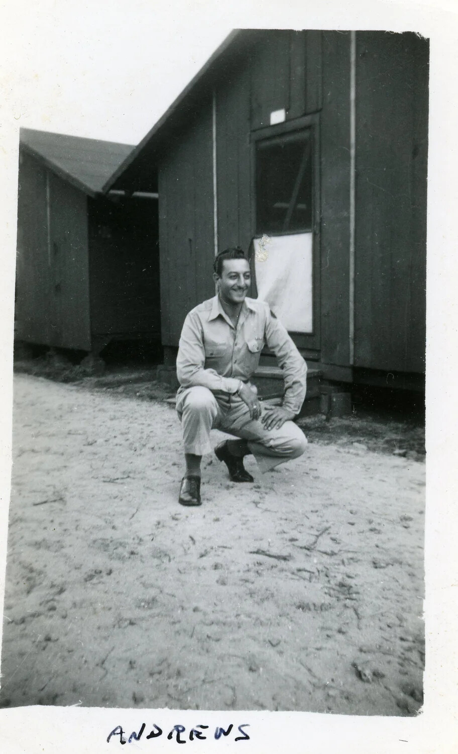 Portrait of Serviceman 'Andrews' Kneeling Before Barracks Building, World War II Era