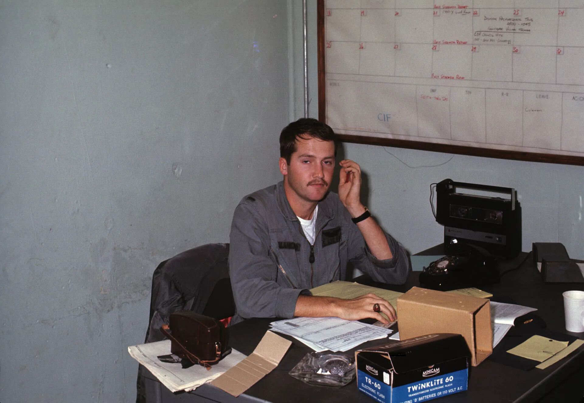 Serviceman at Desk Beneath Training Schedule Board