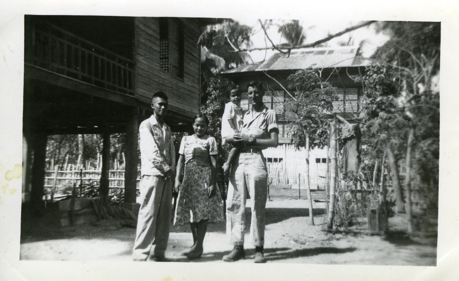 American Serviceman with Okinawan Civilian Family in Front of Traditional Stilt House, Okinawa, 1945