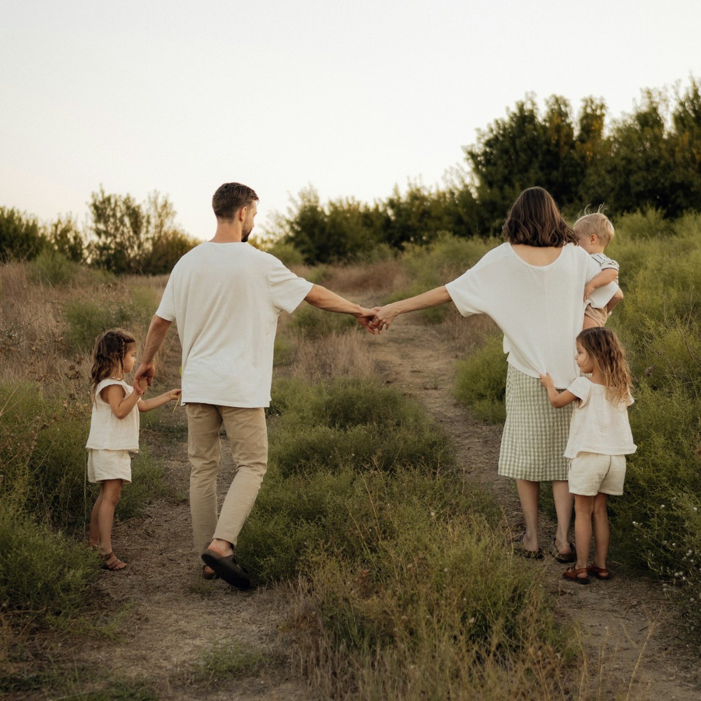 A mom, dad and three young kids walking hand in hand on a grassy hillside path